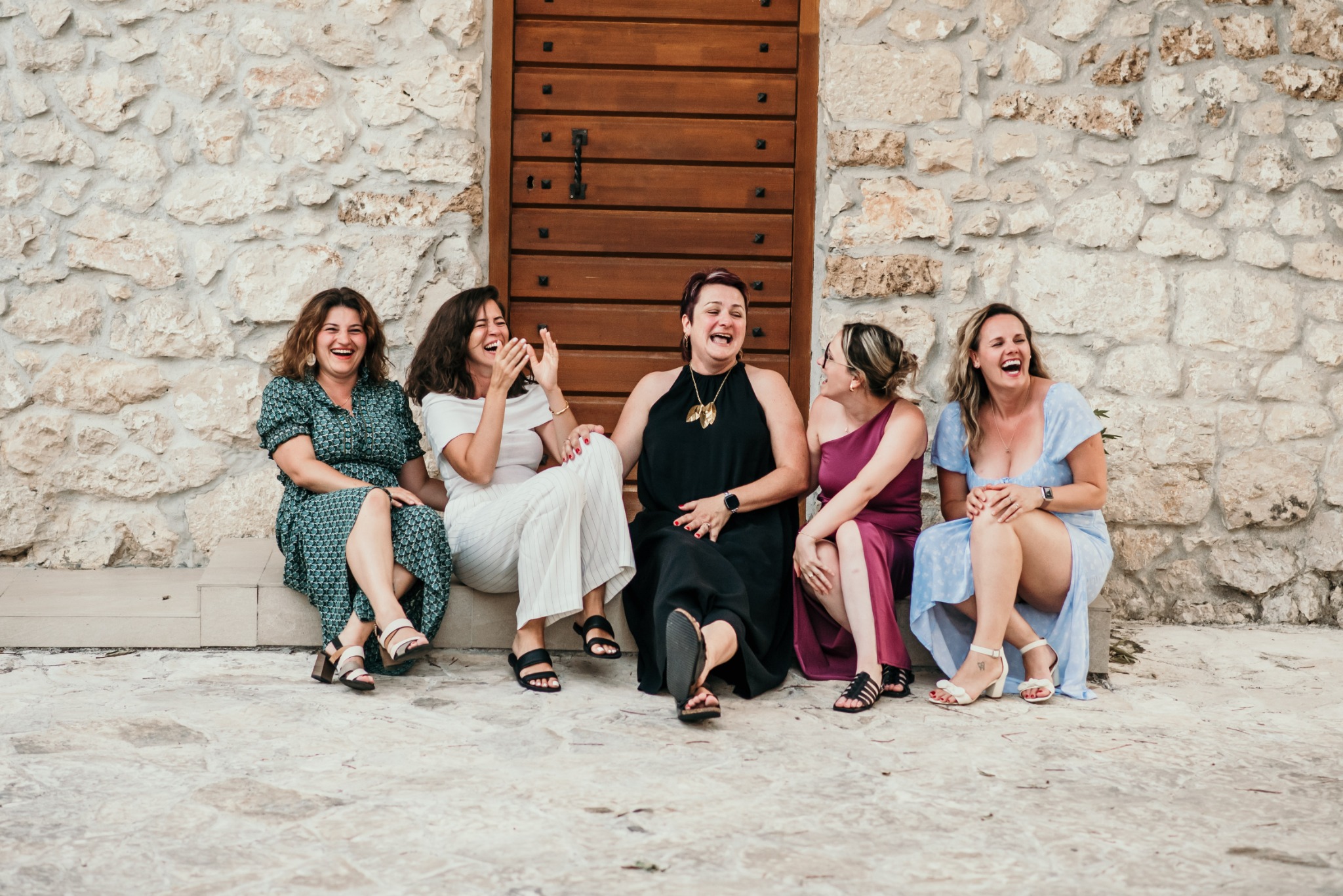 Women sitting together and laughing on stone steps in front of a wooden door
