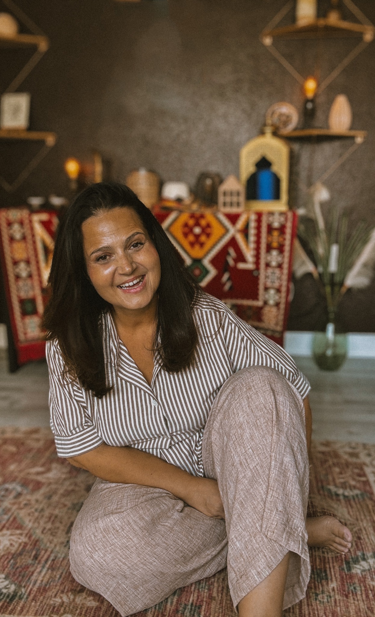 Selma Baćevac smiling in her studio, seated with one knee up